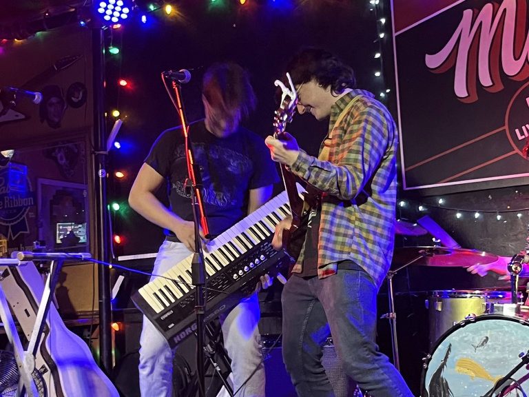 Thor on stage playing a keytar under stage lights, a guitarist beside him