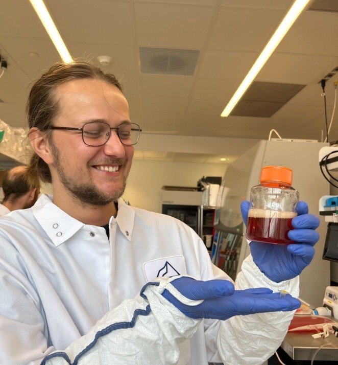 Thor in a lab coat and gloves holding a culture flask, smiling